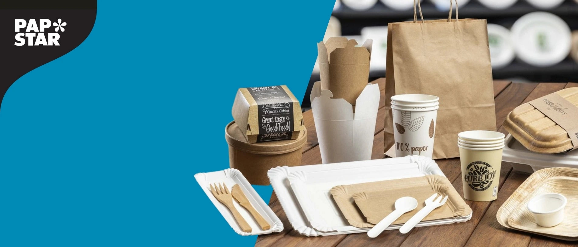 Verschiedene nachhaltige Einwegverpackungen aus Papier und Karton von PAPSTAR, darunter Pappbecher, Take-away-Boxen, Papiertüten, Teller und Holzbesteck, auf einem Holztisch arrangiert. Links ist das PAPSTAR-Logo auf blauem Hintergrund zu sehen.“