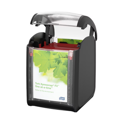 A Tork Xpressnap Fit® 272900 table dispenser for napkins by the brand TORK, Essity Professional Hygiene Germany GmbH, with an open top. This black dispenser features a clear front display with a green leaf design that promotes "one-at-a-time" use to reduce napkin consumption and emphasizes that it is "better for the environment."