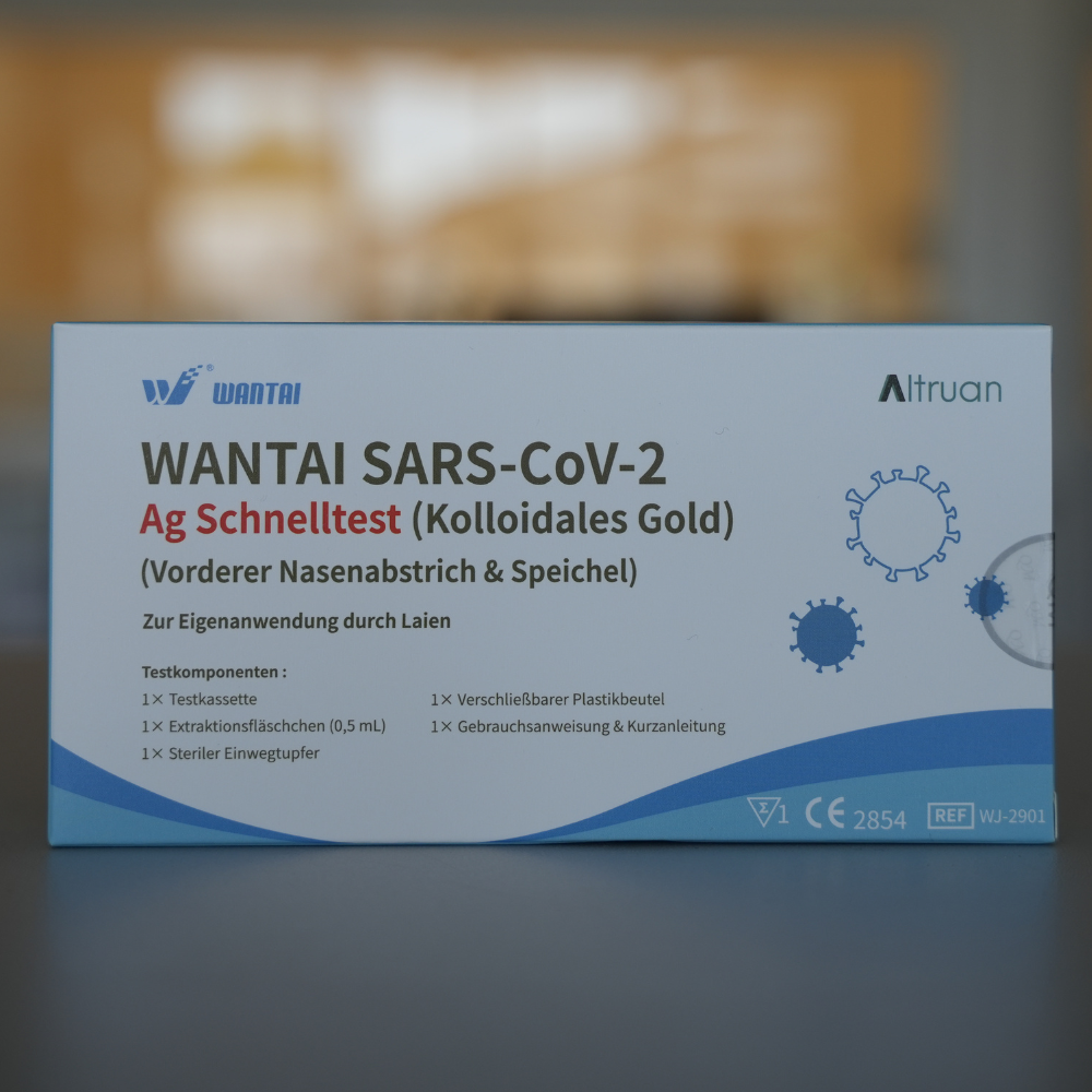 A box of Wantai SARS-Cov-2 rapid test, lollipop test (Colloidal Gold) CE/2854 is displayed. The packaging is blue and white with a diagram of the virus and German text describing the test for nasal and saliva samples. The CE and Altruan logos are clearly visible.