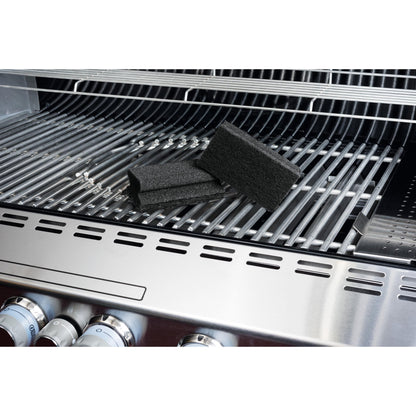 A Scotch-Brite® Grill Handle Sponge from 3M Deutschland GmbH lies on a stainless steel grill, highlighting easy grill cleaning. The black sponges, grill knobs, and the opened lid are visible on the rack.
