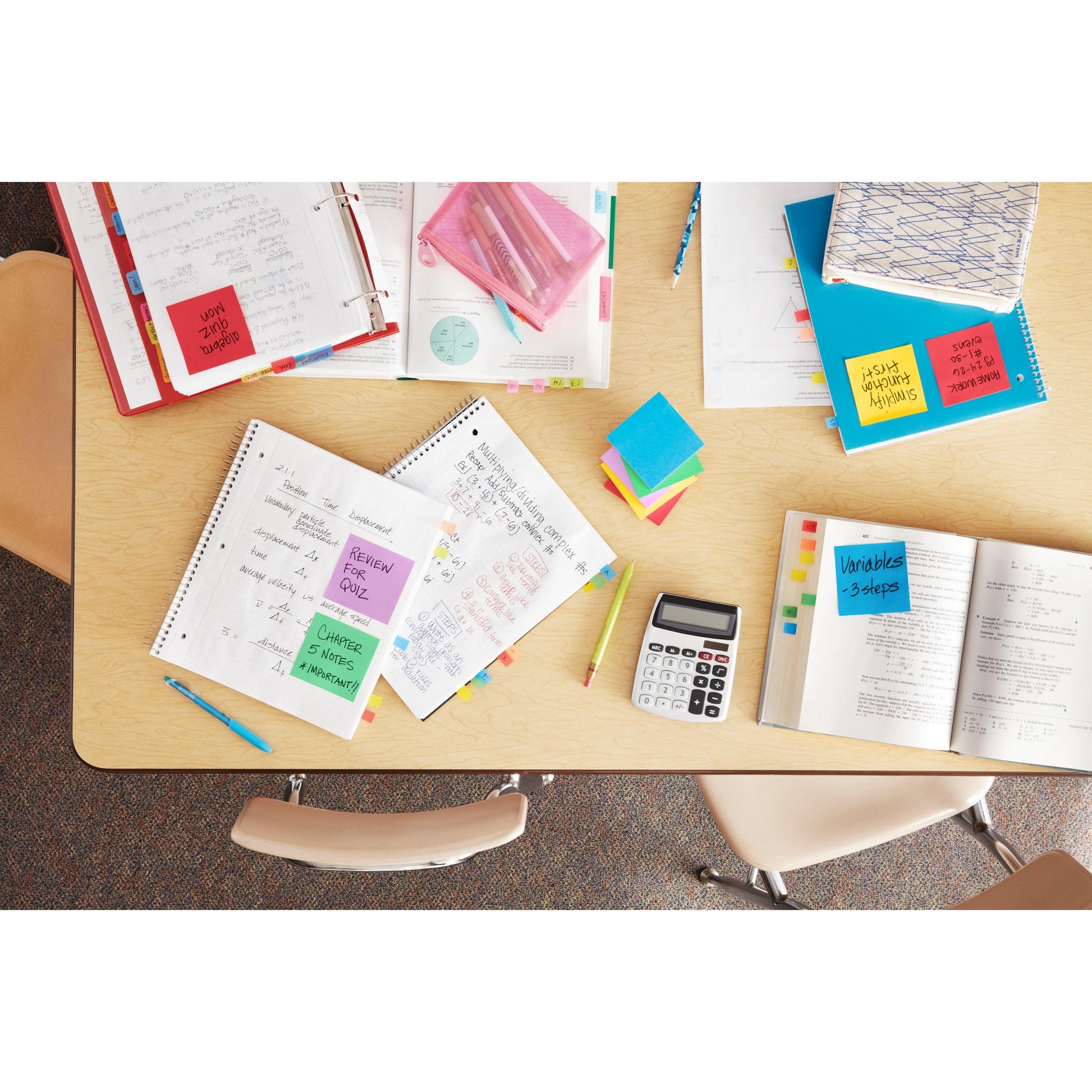 Ein Tisch im Klassenzimmer mit aufgeschlagenen Heften, Lehrbüchern, Ordnern, einem Taschenrechner, Stiften, Textmarkern und bunten Post-it® Super Sticky Z-Notes (Neonfarben) von 3M Deutschland GmbH. Zwei Stühle sind vorhanden; die Materialien lassen auf Lernen oder Prüfungsvorbereitung schließen.
