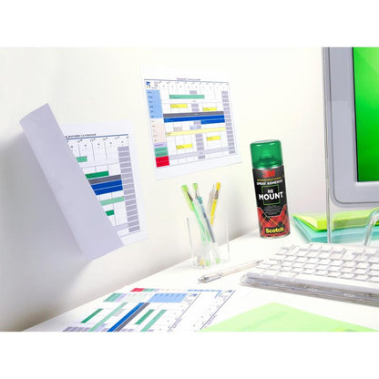 A computer monitor stands on a white desk with maps, papers, pens in a holder, and a can of 3M™ Scotch® ReMount™ adhesive spray (400 ml, 1 can/package) from 3M Deutschland GmbH. Above it, two maps are temporarily attached to the wall.