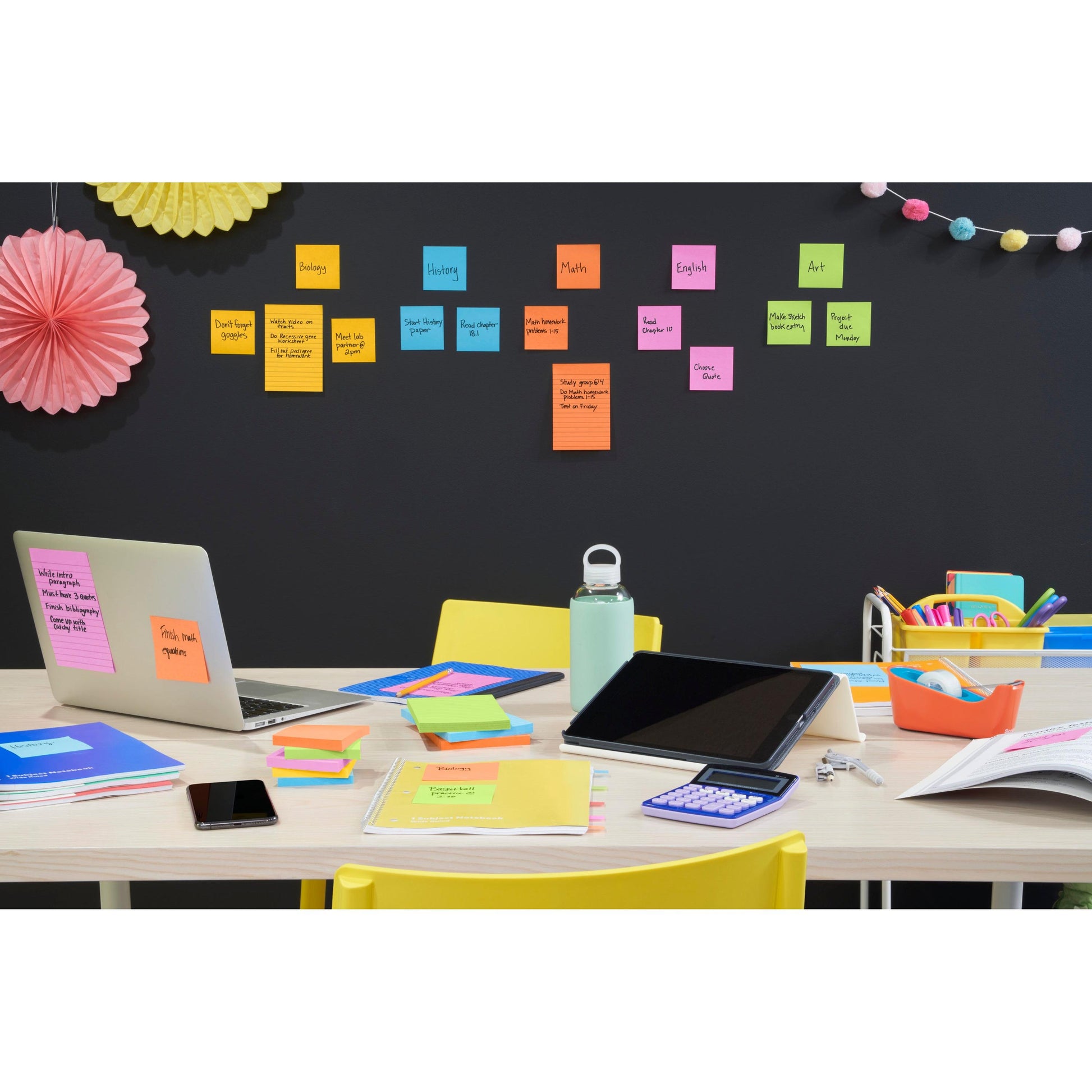 Ein Arbeitsbereich im Klassenzimmer ist mit Laptop, Tablet, Notebook, Taschenrechner, Telefon, Wasserflasche und Post-it® Super Sticky Notes (76 mm x 76 mm, 90 Blatt/Block) der 3M Deutschland GmbH ausgestattet, farblich sortiert nach Schulfächern wie Biologie und Mathematik.