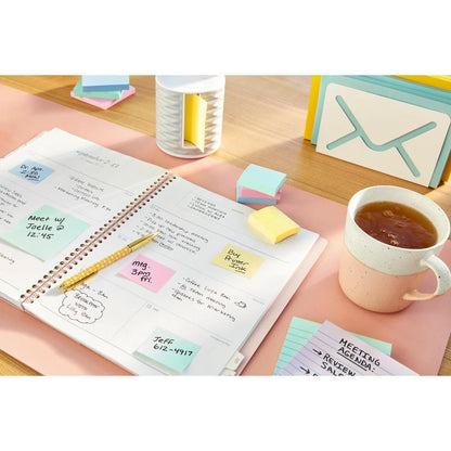 An open planner shows a weekly schedule on a desk, surrounded by handwritten notes, a pen, office supplies, small cards, a cup of tea, and Post-it® Recycling Notes (38 mm x 51 mm) from 3M Deutschland GmbH.