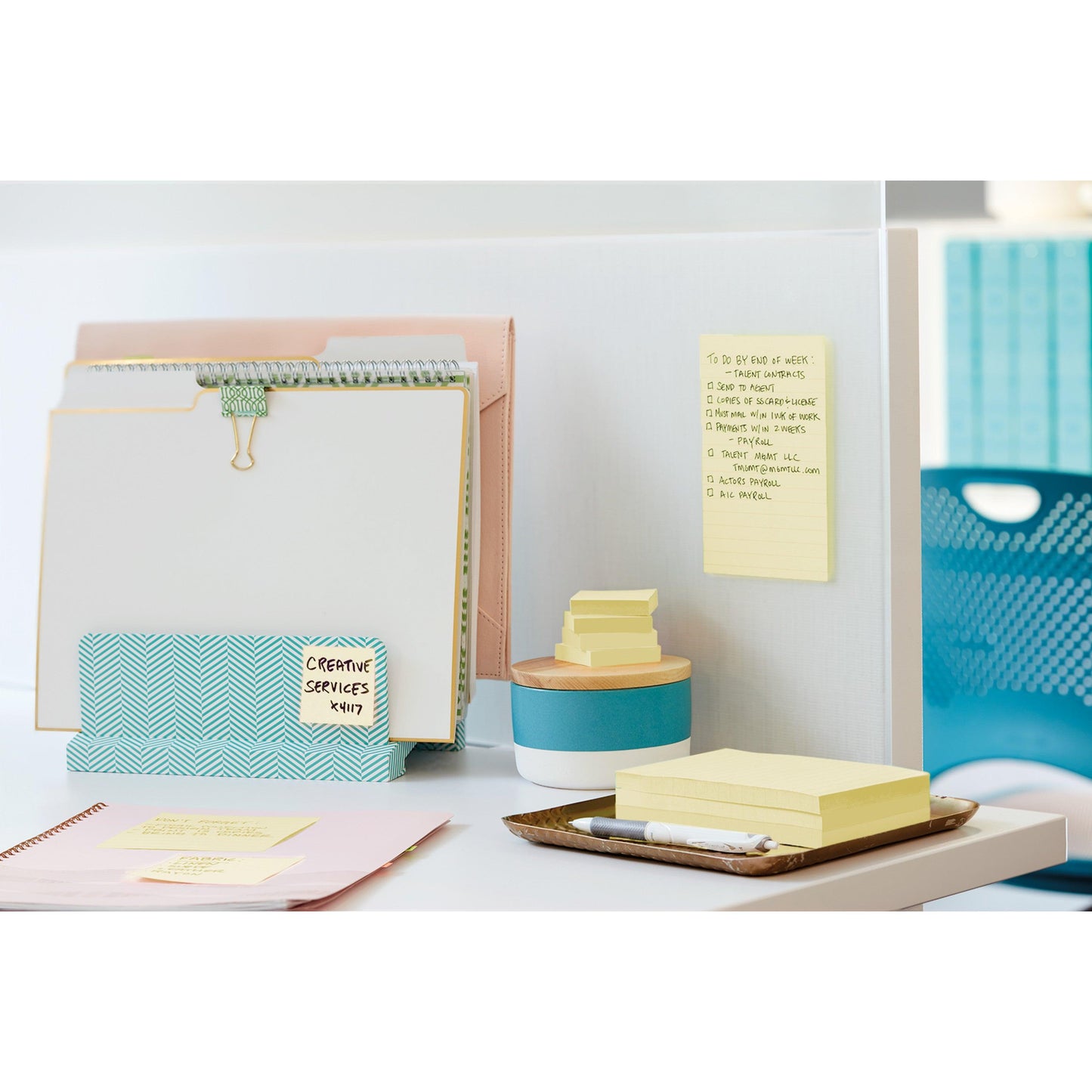 A tidy desk with binders, a notepad, 3M Post-it® Super Sticky Notes Yellow (47.6x47.6 mm, 21+3 Promo Pack), a pen, a small box, a tablet; a task list is attached to the partition. A blue office chair stands in the background.
