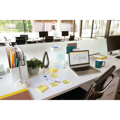 On a modern office table are a laptop, 3M Post-it® Notes (Yellow, 51x76mm, 100 sheets/pad, 12 pads/pack, PEFC-certified), papers, pens, a mug, and a plant. Empty desks and large windows fill the bright background.