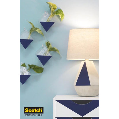 A lamp with a geometric base stands on a white dresser with blue triangles; four wall-mounted triangular planters with green plants hang on a light blue wall. The 3M Scotch® painter's masking tape for delicate surfaces logo appears in the lower left corner.