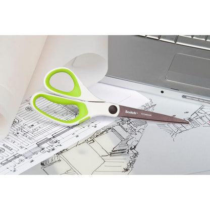 A pair of Scotch™ titanium scissors, 20 cm from 3M Deutschland GmbH, with white and green handles, rests on architectural drawings next to a silver laptop and a roll of tracing paper.