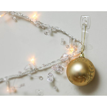 A golden Christmas ornament hangs on a Command™ Mini Hook, transparent, with transparent strips, 17006CLR from 3M Deutschland GmbH, next to illuminated white lights and clear crystals on a white wall.