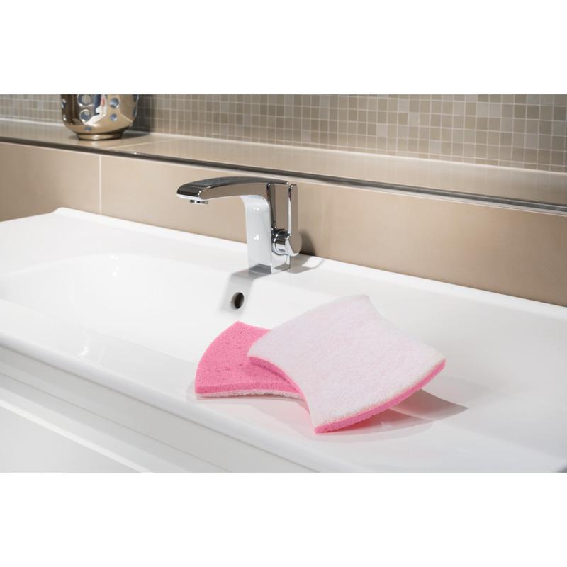 A white sink with a chrome faucet shows the Scotch-Brite® Bath XXL cleaning sponge from 3M Deutschland GmbH, pink on one side and white on the other, ideal for removing limescale deposits. Beige and light brown tiles appear in the background.