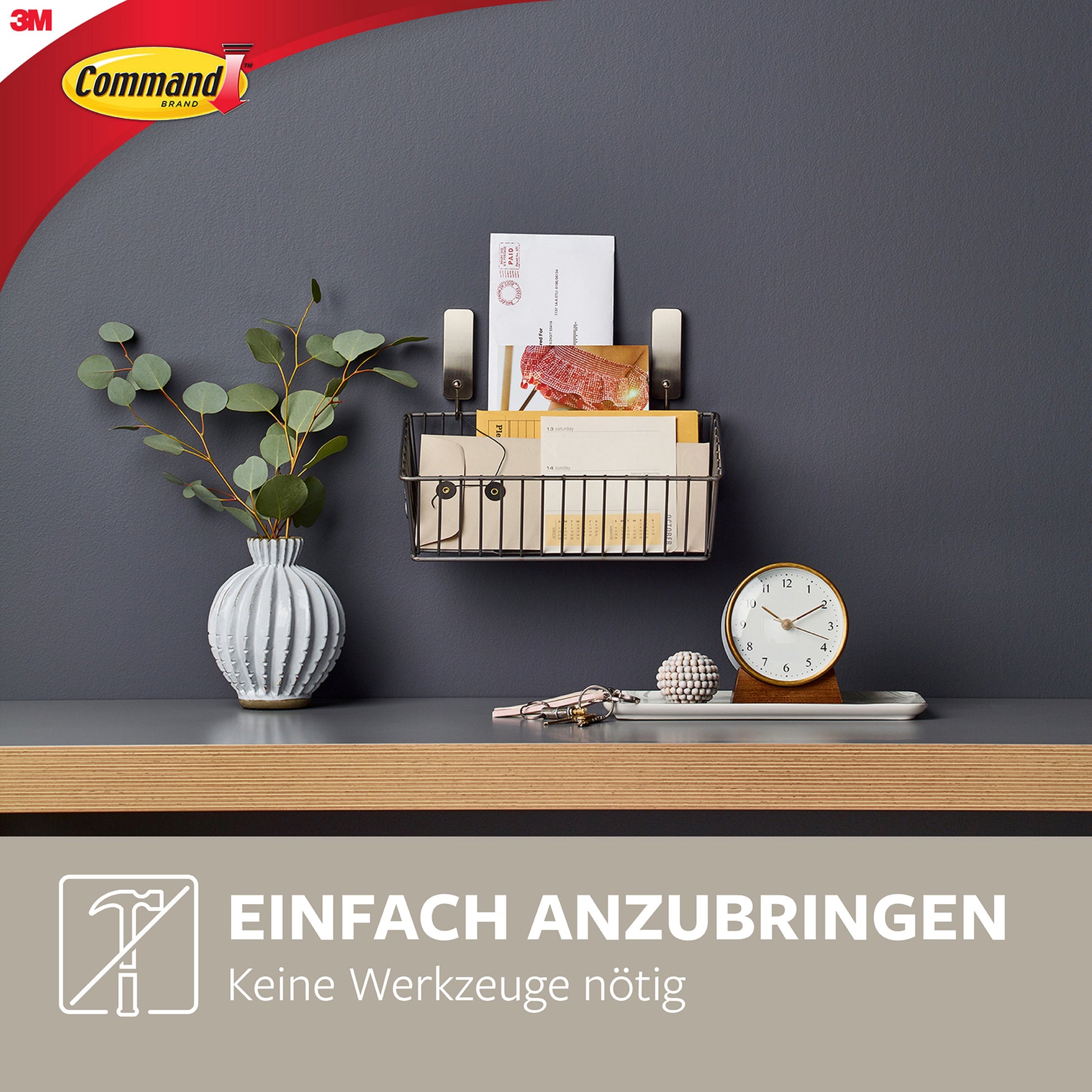 An einer grauen Wand über einem hölzernen Schreibtisch wird mit einem 3M Deutschland GmbH Mittelgroßer Command™ Metallhaken in gebürstetem Nickel, 17034, ein Wandorganizer aus Metall mit Briefen und Briefumschlägen angebracht - die Montage erfolgt werkzeuglos.
