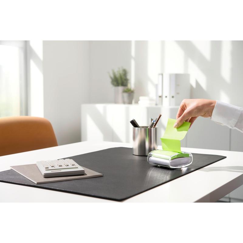 A person pulls a yellow Post-it® Super Sticky Z-Note (76 x 76 mm) from the black PRO Post-it® Z-Notes Dispenser from 3M Deutschland GmbH, on a tidy desk with a calculator, pen holder, and black pad in bright daylight.